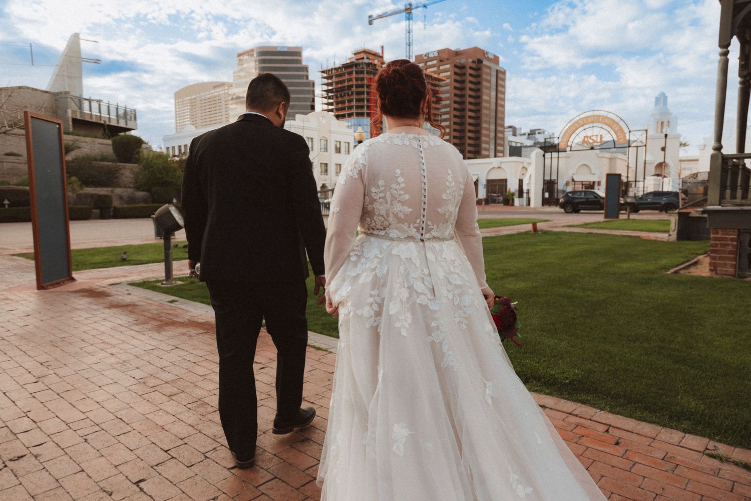 A wedding couple walks towards historic buildings in an urban setting.