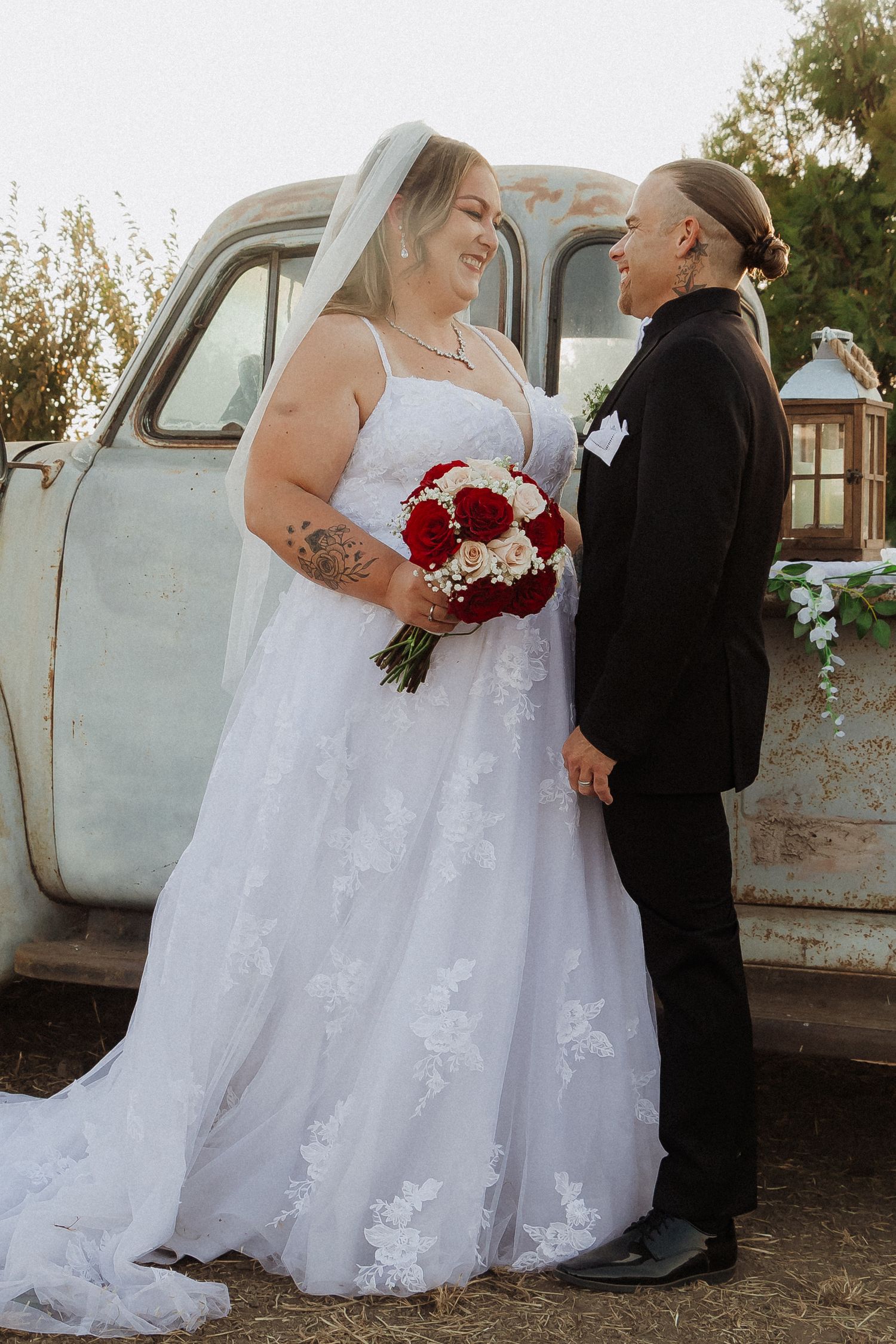 A romantic wedding portrait beside a vintage blue truck with a red and white bouquet.