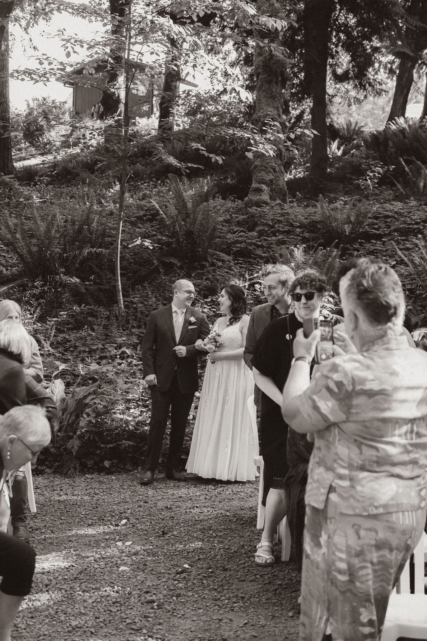 A wedding ceremony taking place on a wooded path with guests gathered around.