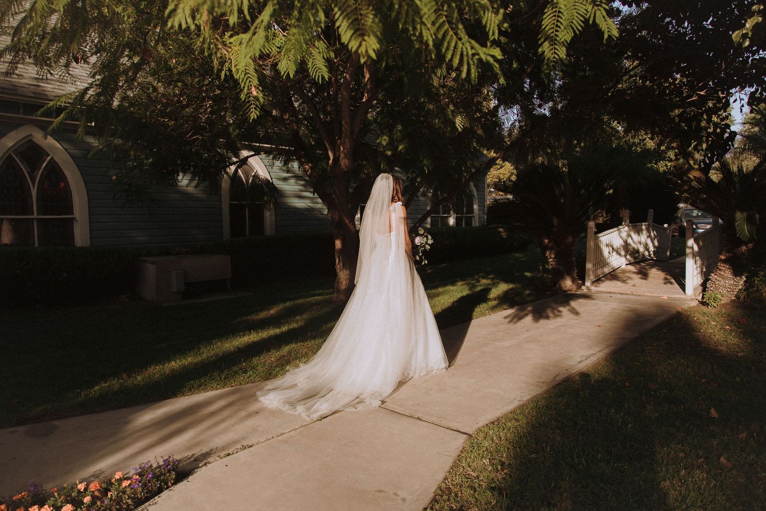 Wedding dress silhouette in afternoon sunlight walking along church pathway.