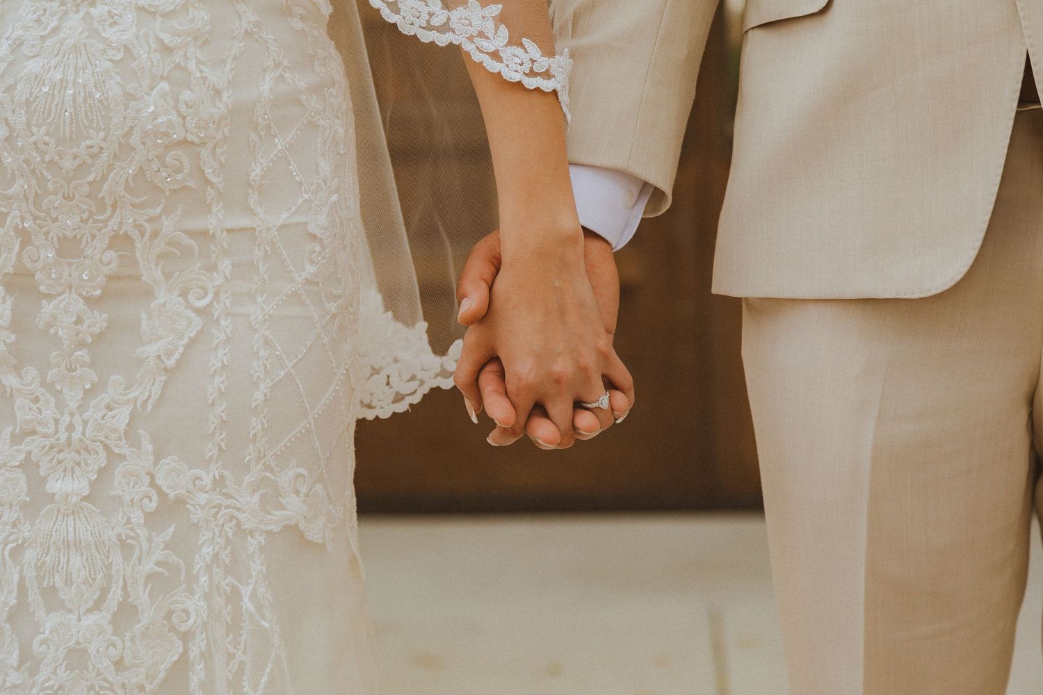 Close-up of couple's intertwined hands showing wedding attire details.