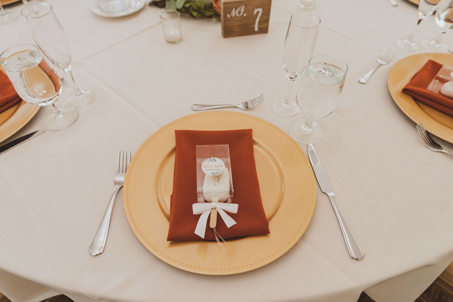 Formal place setting with gold charger plate, burgundy napkin and table number display.