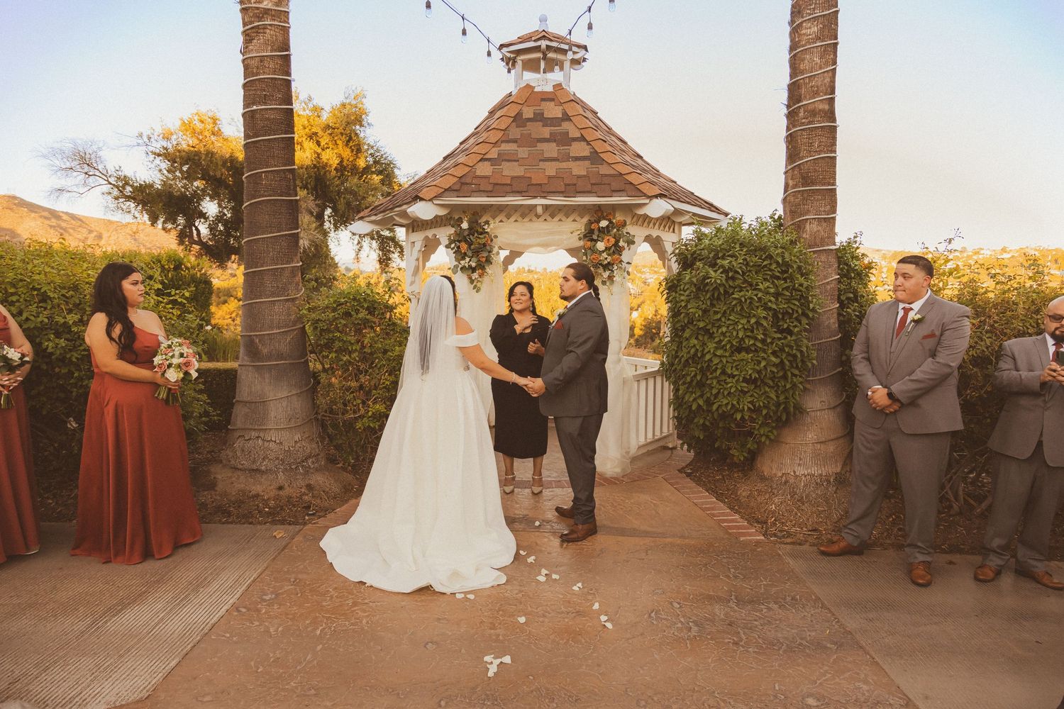 Beautiful outdoor wedding ceremony at a gazebo surrounded by palm trees and string lights.