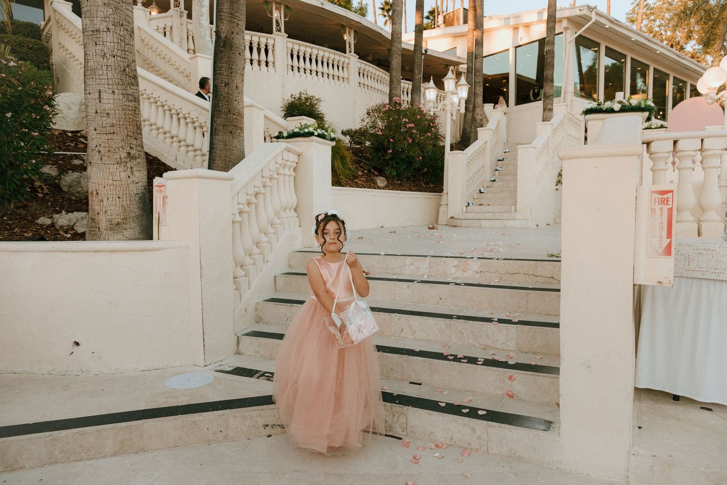 Person in blush tulle gown poses gracefully on white architectural staircase.