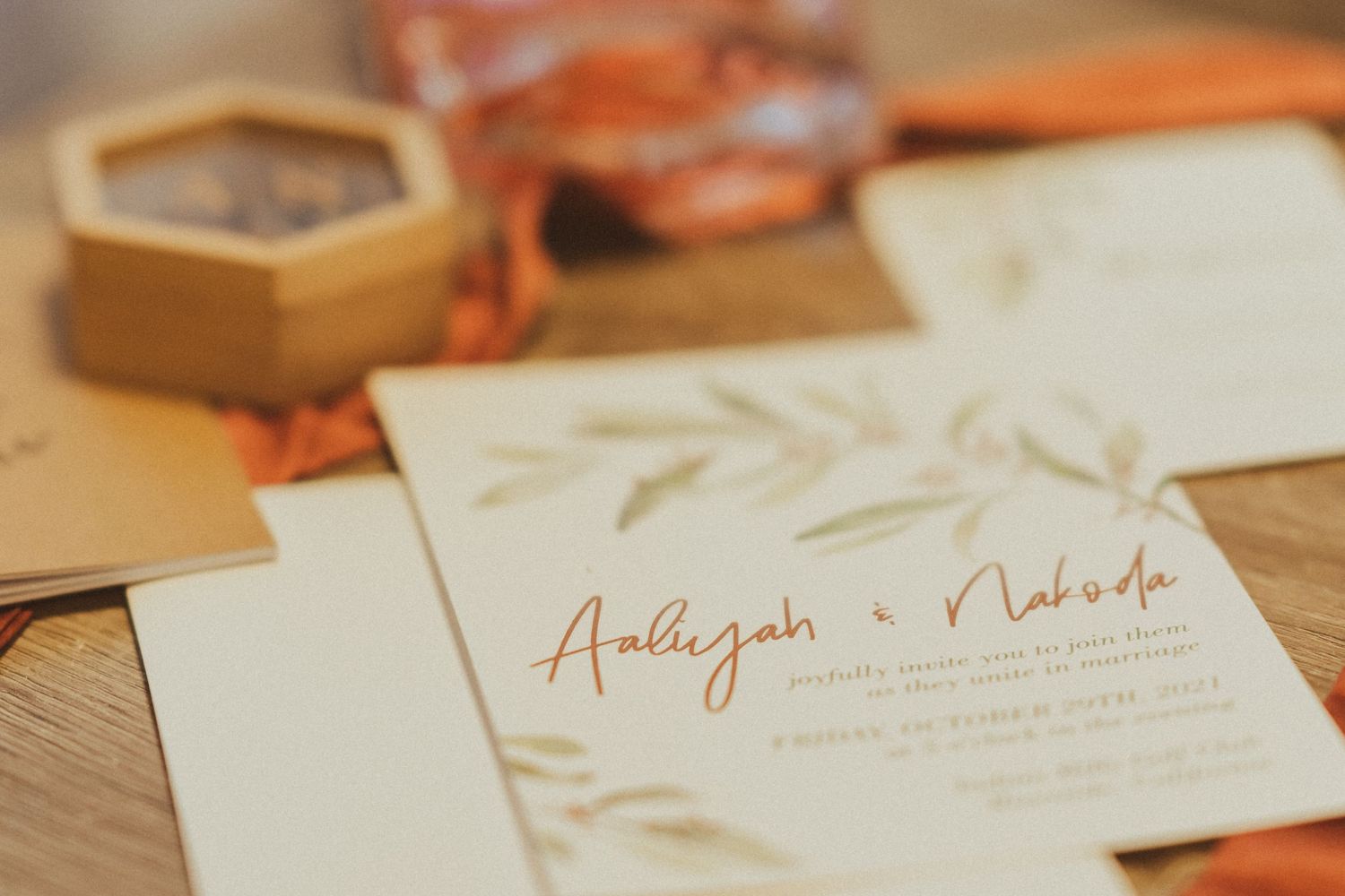 Detailed shot of wedding invitation with copper calligraphy and olive leaf design.