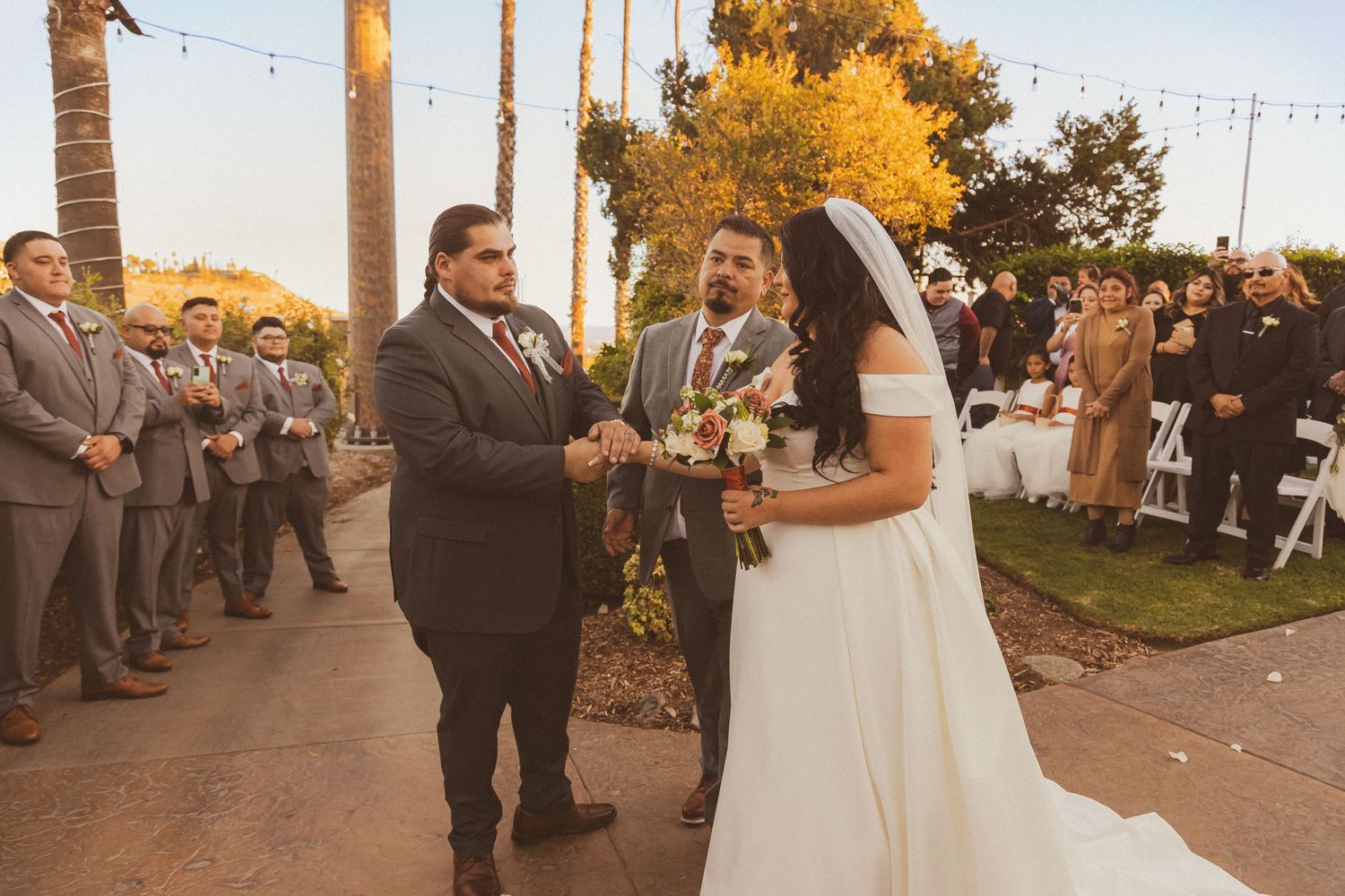 Wedding ceremony under string lights with palm trees and golden sunset backdrop.