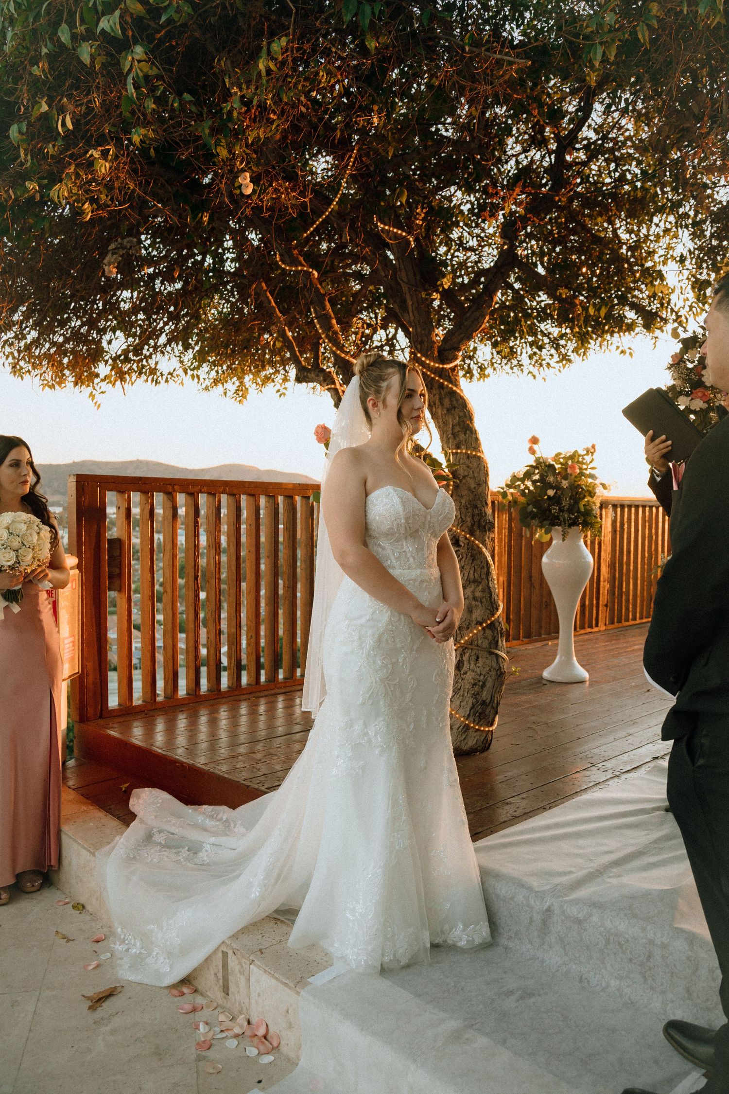 An outdoor wedding ceremony on a wooden deck with string lights and floral arrangements.