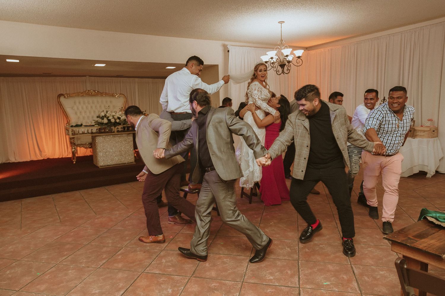 Wedding guests jump and dance energetically in synchronization at an indoor reception.