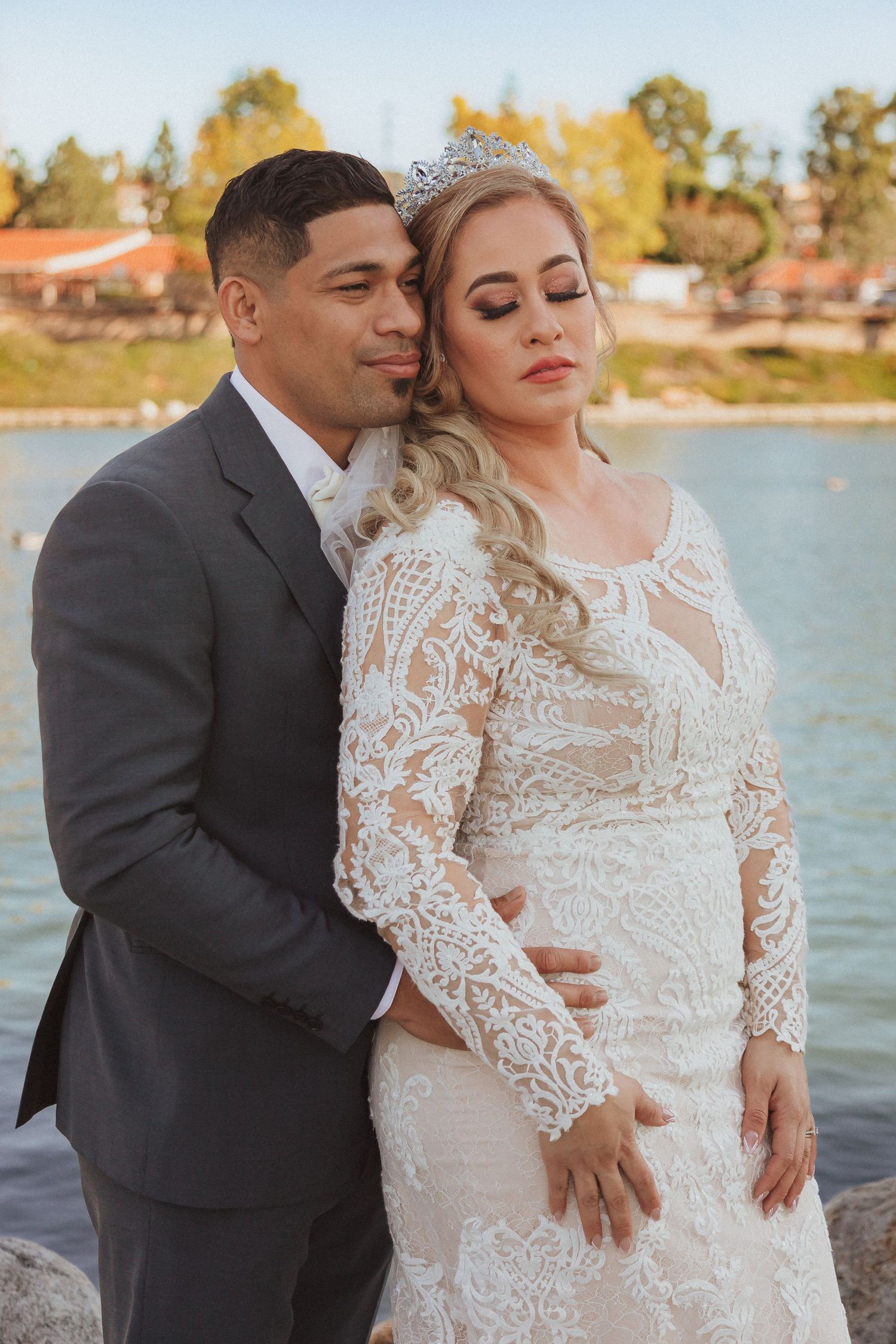 Wedding couple poses together by waterfront in formal attire.