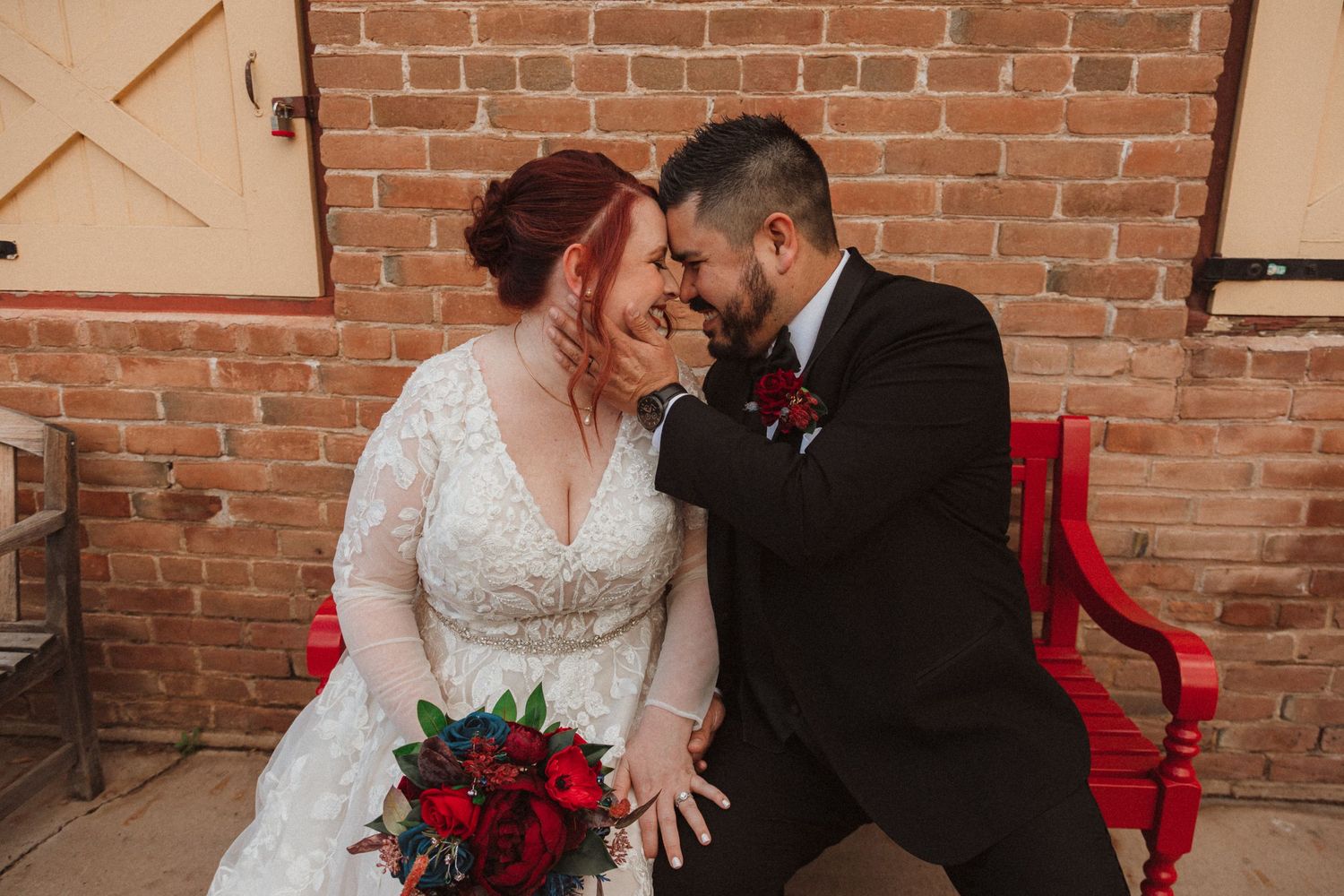 A romantic wedding moment captured against a brick wall backdrop with red accents.