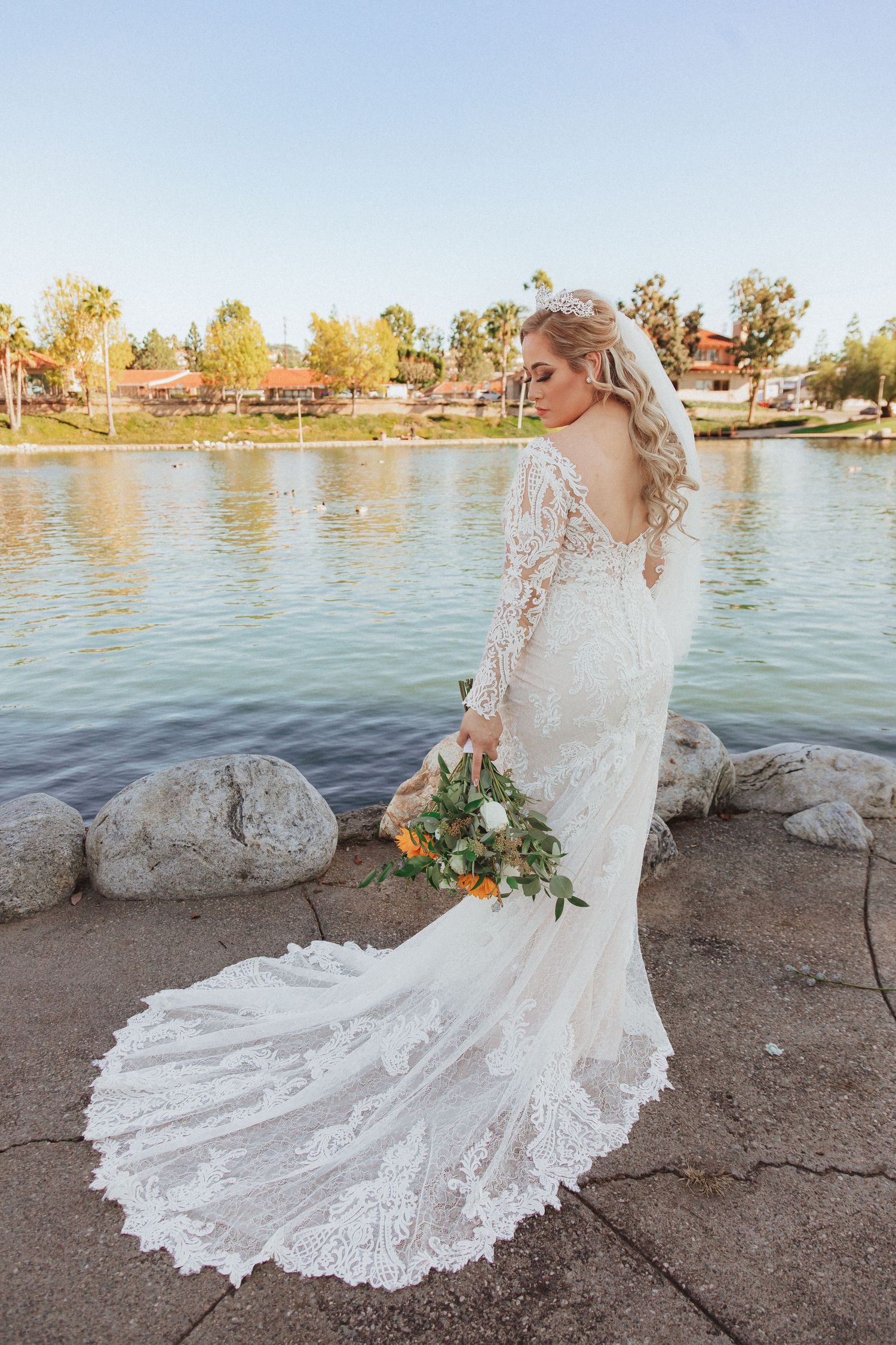 Elegant bridal portrait showing flowing lace train and autumn lakeside scenery.