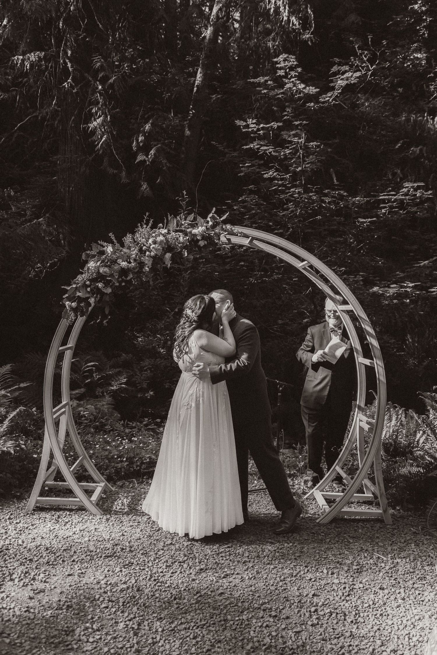 A black and white photo of a couple dancing under a circular wedding arch.