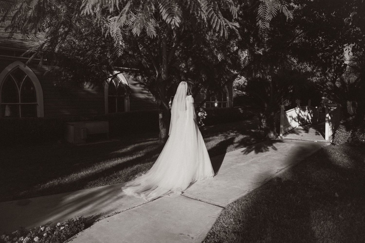 Black and white photo of flowing wedding dress and veil against dramatic shadows.