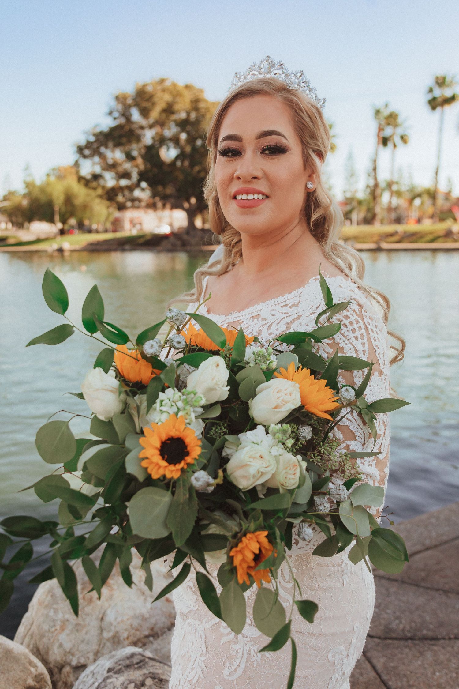 Beautiful wedding bouquet featuring sunflowers and white roses against lakeside backdrop.