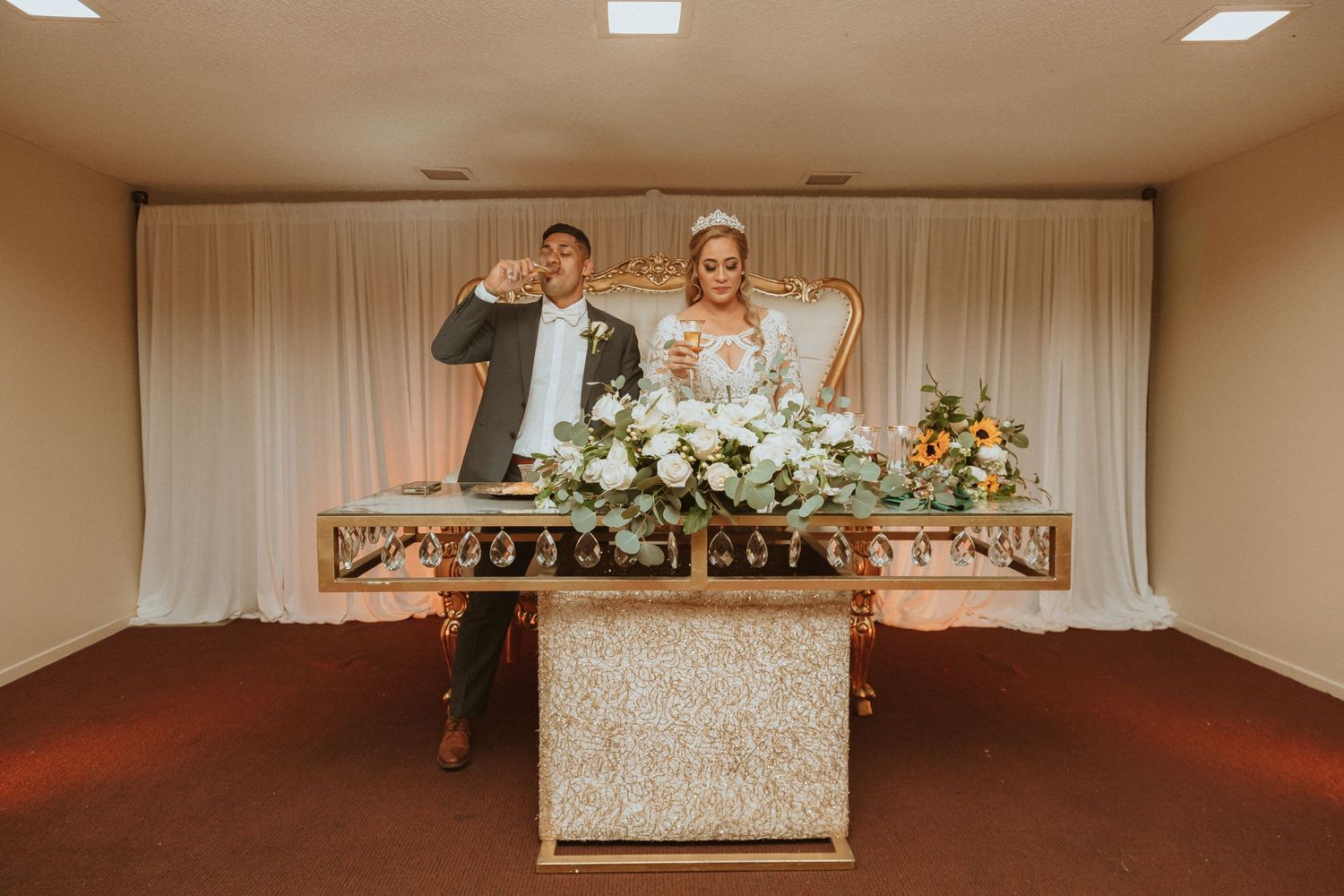 Joyful celebration captured during wedding reception behind decorated sweetheart table.