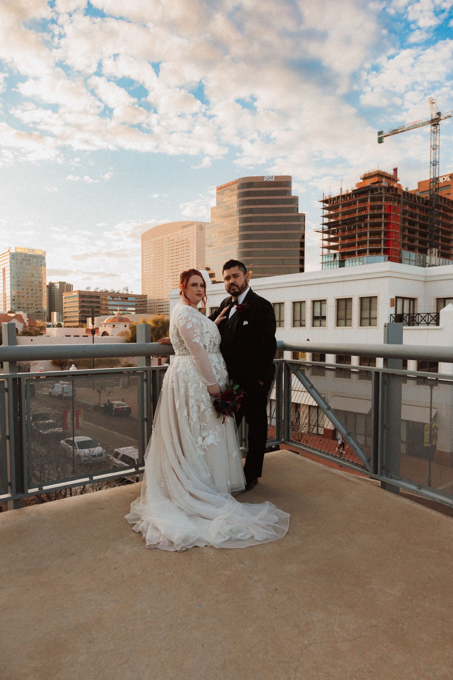 Wedding couple poses on a city rooftop terrace with construction cranes and skyscrapers visible behind them.