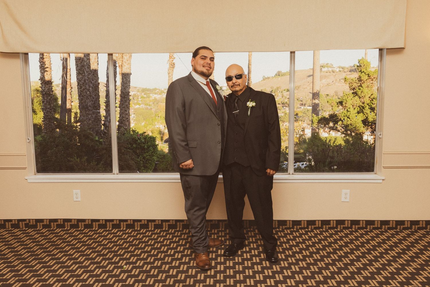 Special moment between two people in formal attire standing by a window in warm lighting.