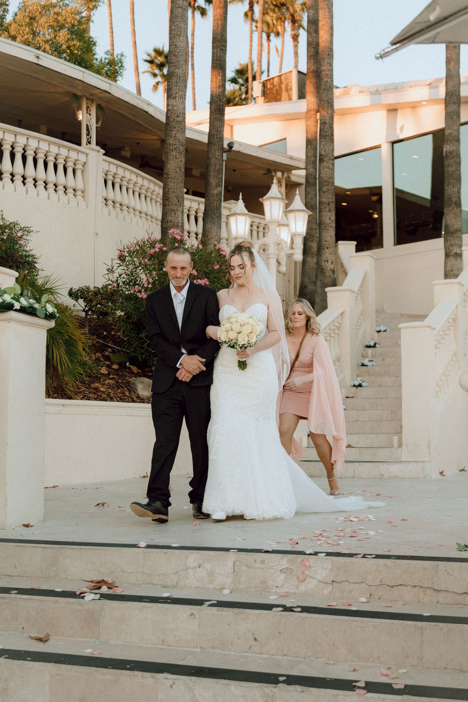 Elegant outdoor wedding photo on white stone steps with palm trees in background.
