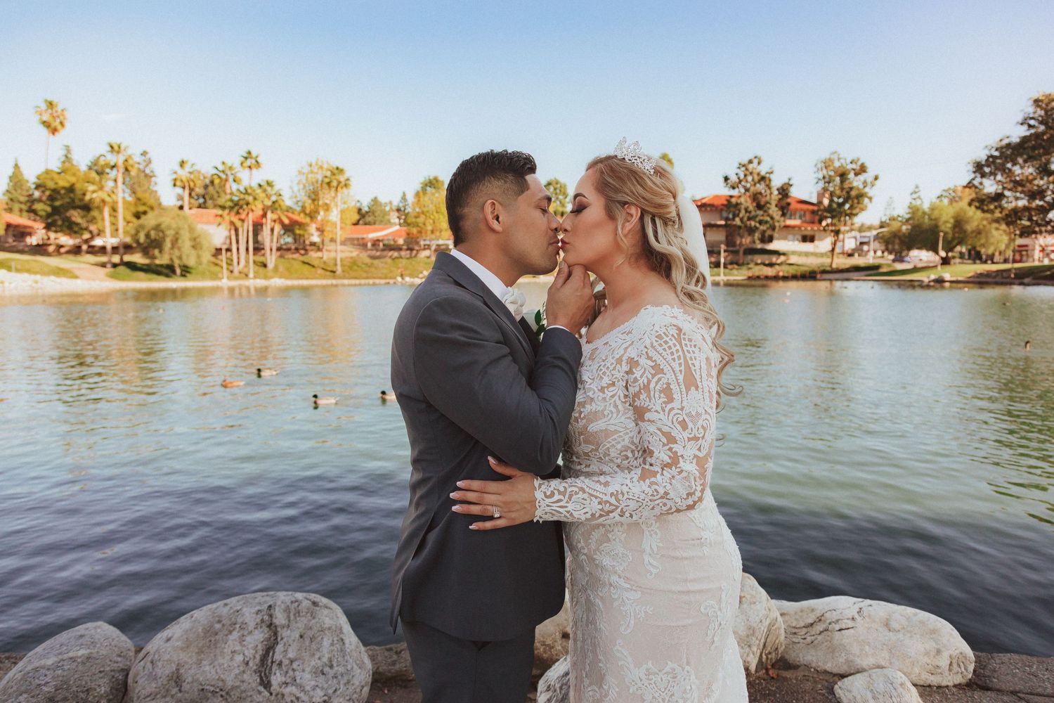 A tender kiss between newlyweds against a serene lake backdrop during their wedding.