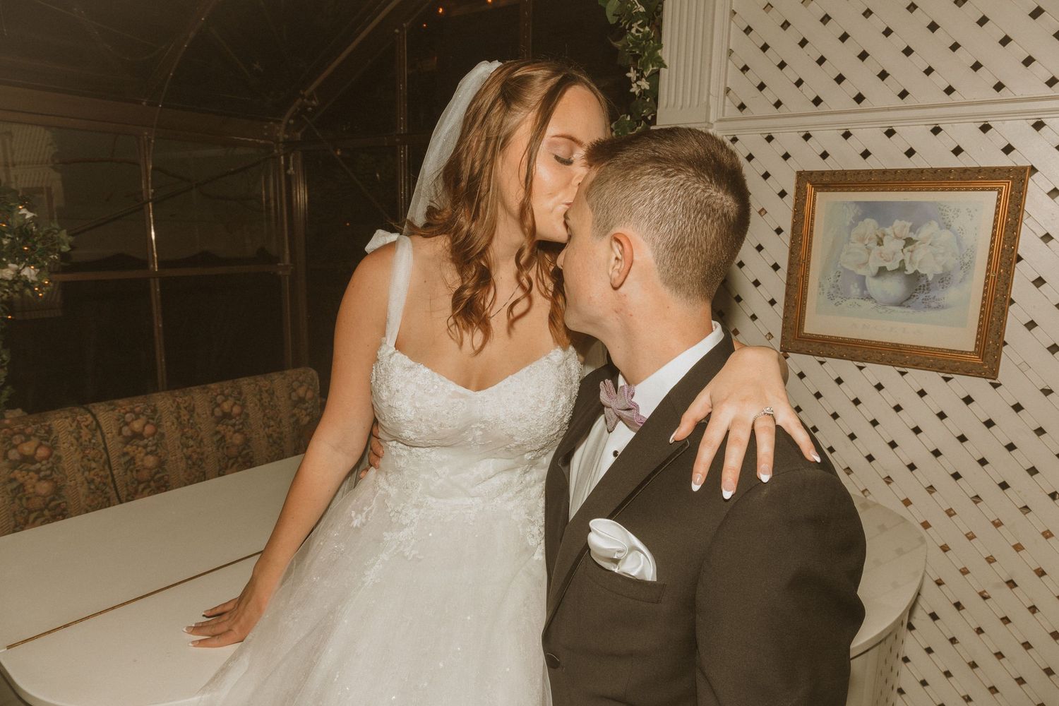 Newlyweds share an intimate moment during their wedding reception in front of a white lattice backdrop.