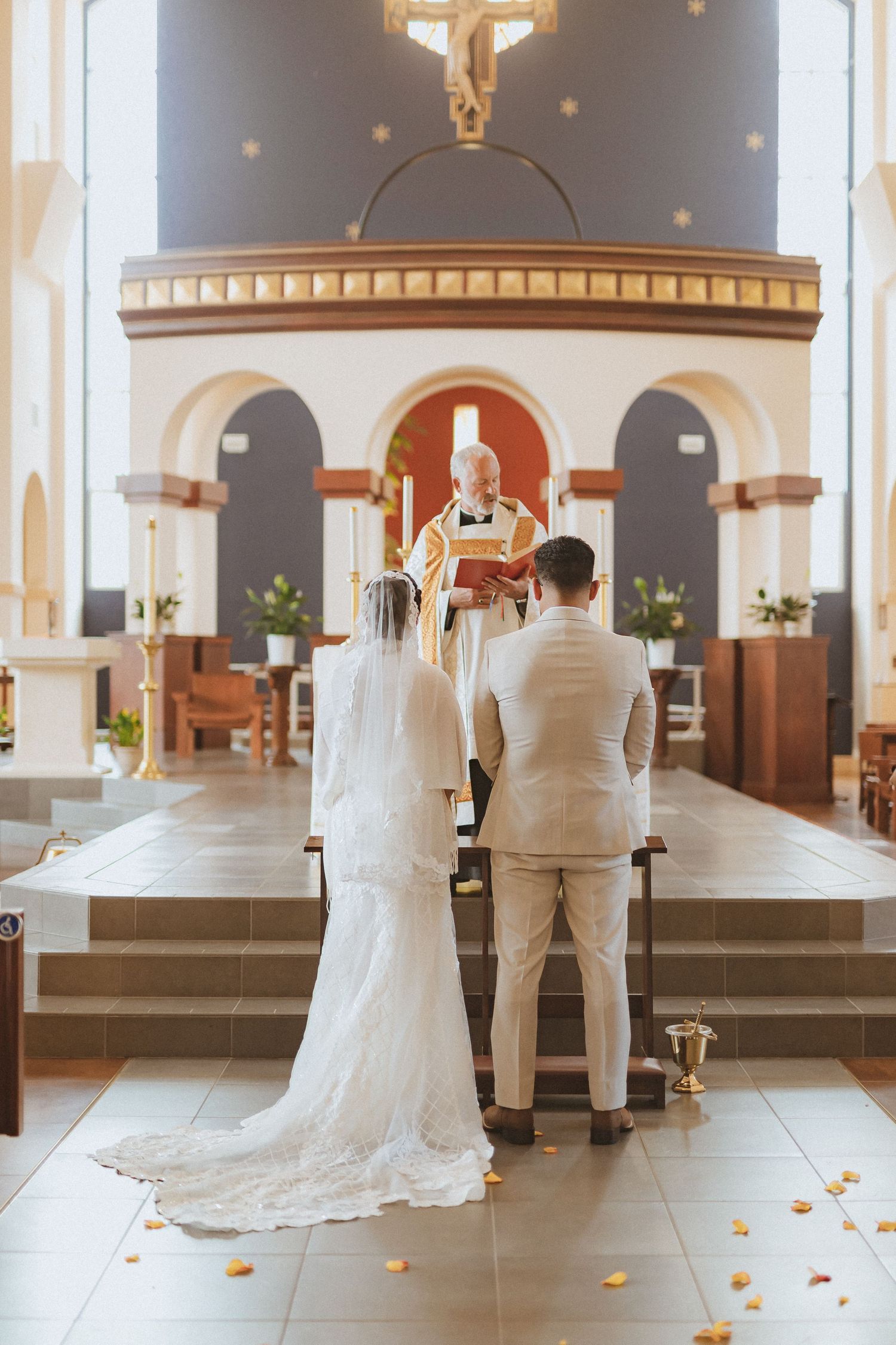 A couple stands before the altar during their wedding ceremony beneath a mounted crucifix.