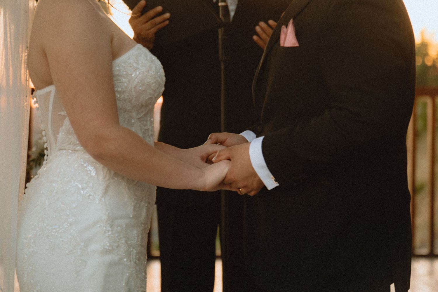 Close-up of couple holding hands during sunset wedding ceremony.