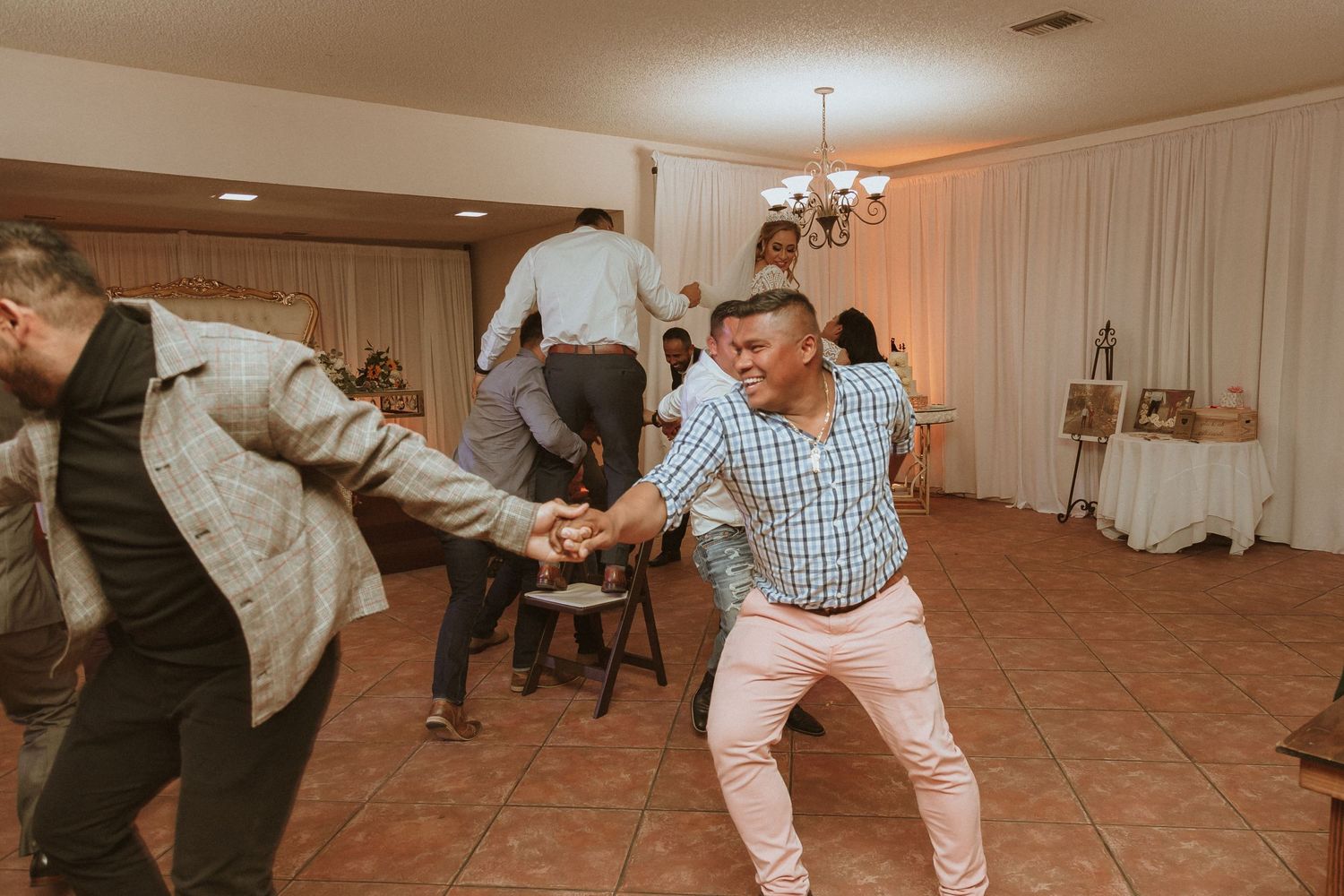 Wedding guests dance energetically on a tiled floor during a reception celebration.