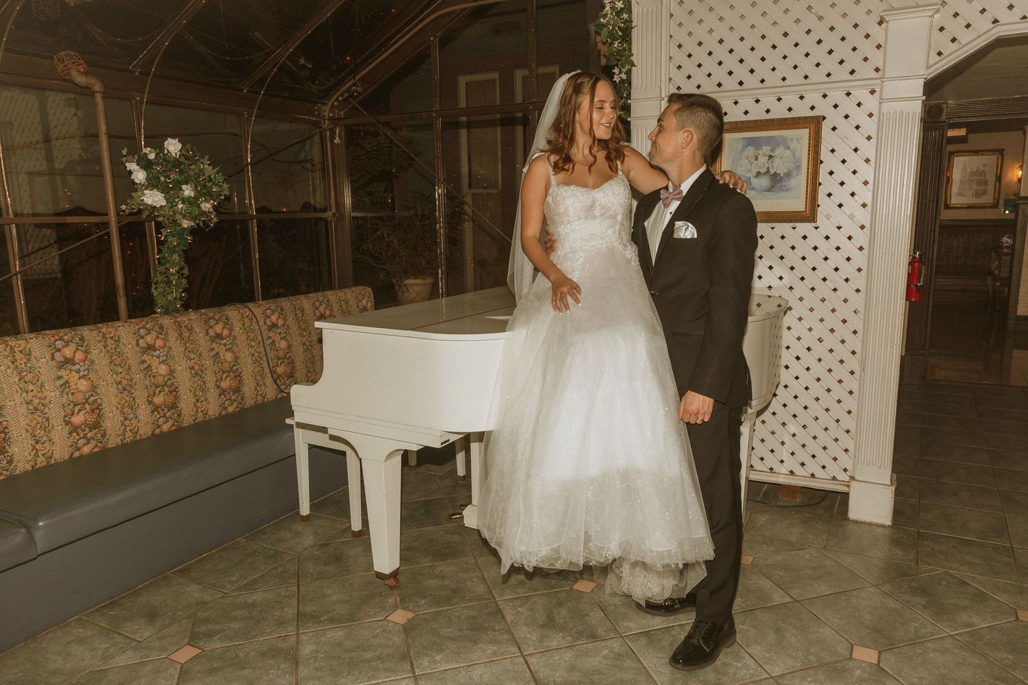 Rustic indoor wedding scene with couple standing next to a white piano and lattice backdrop.