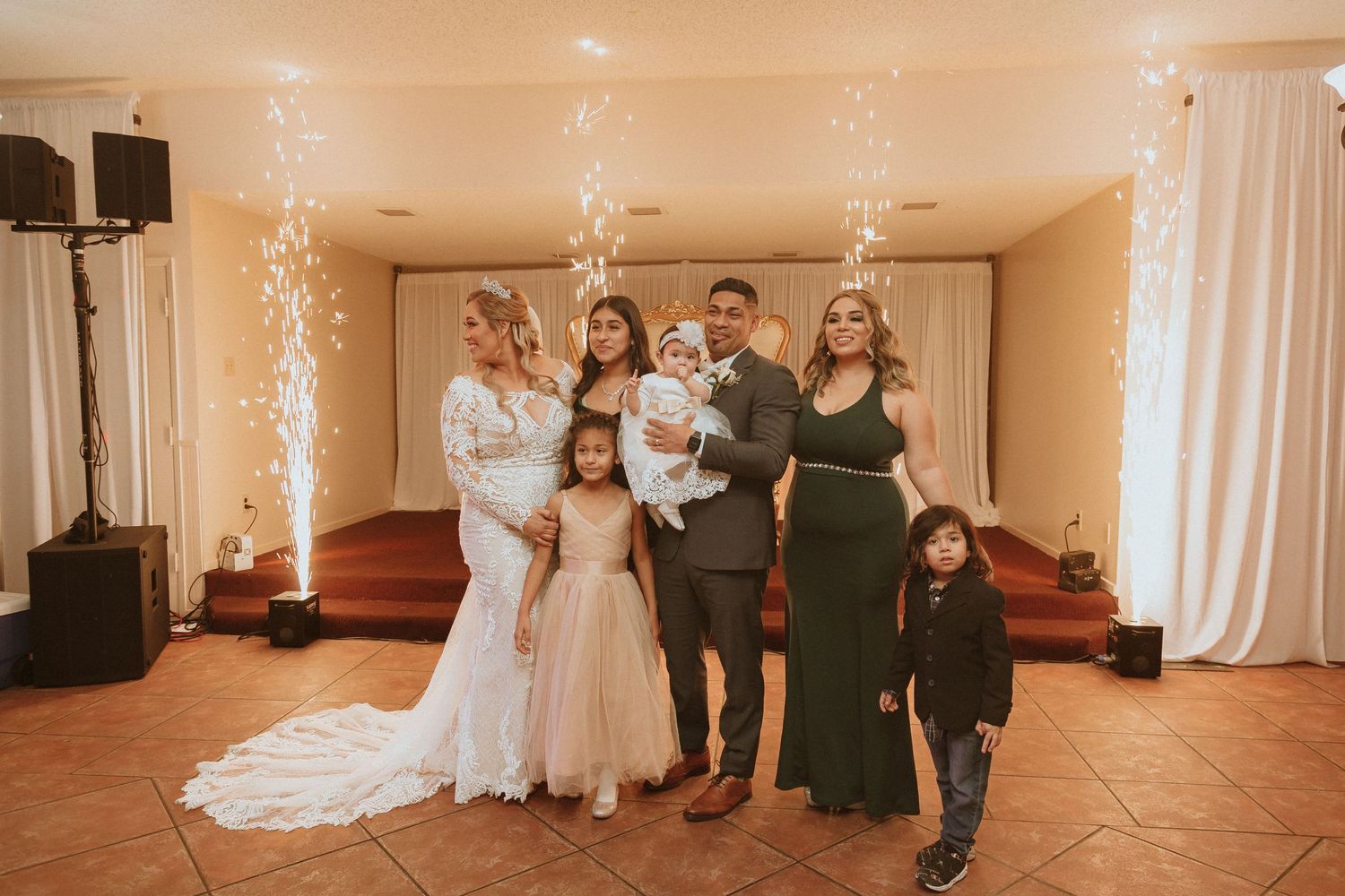 A wedding group photo with family members dressed in formal attire against a backdrop with sparkler effects.