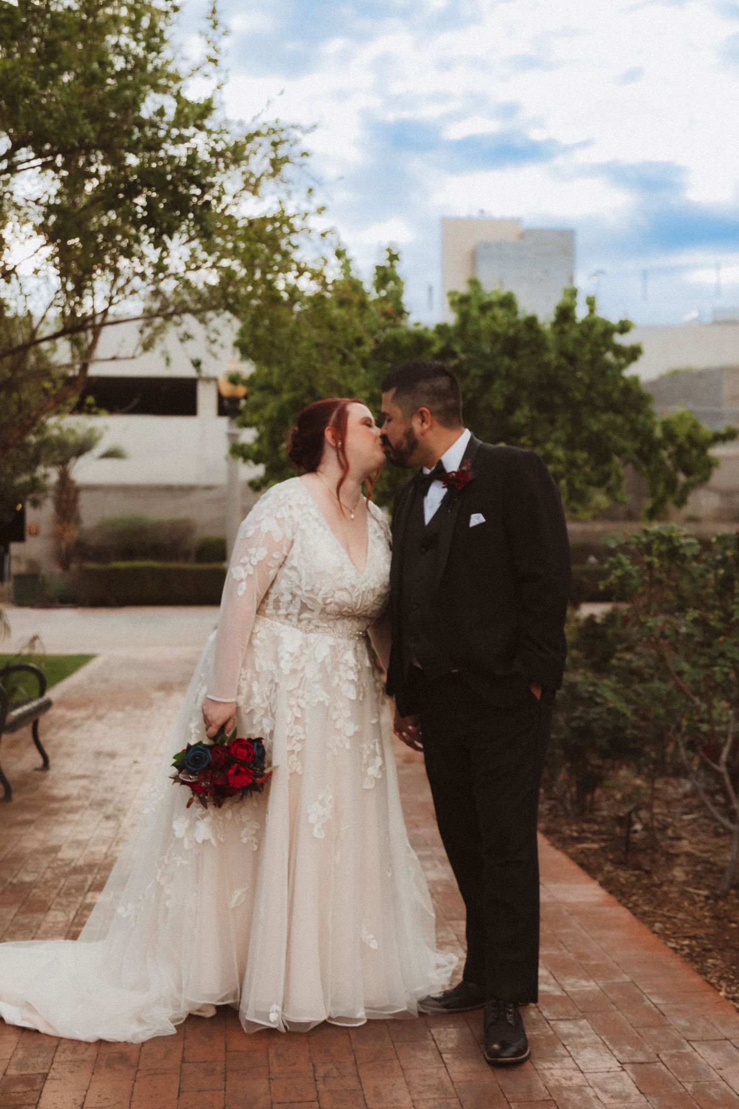 An intimate wedding portrait captured on a brick pathway with trees and buildings in background.