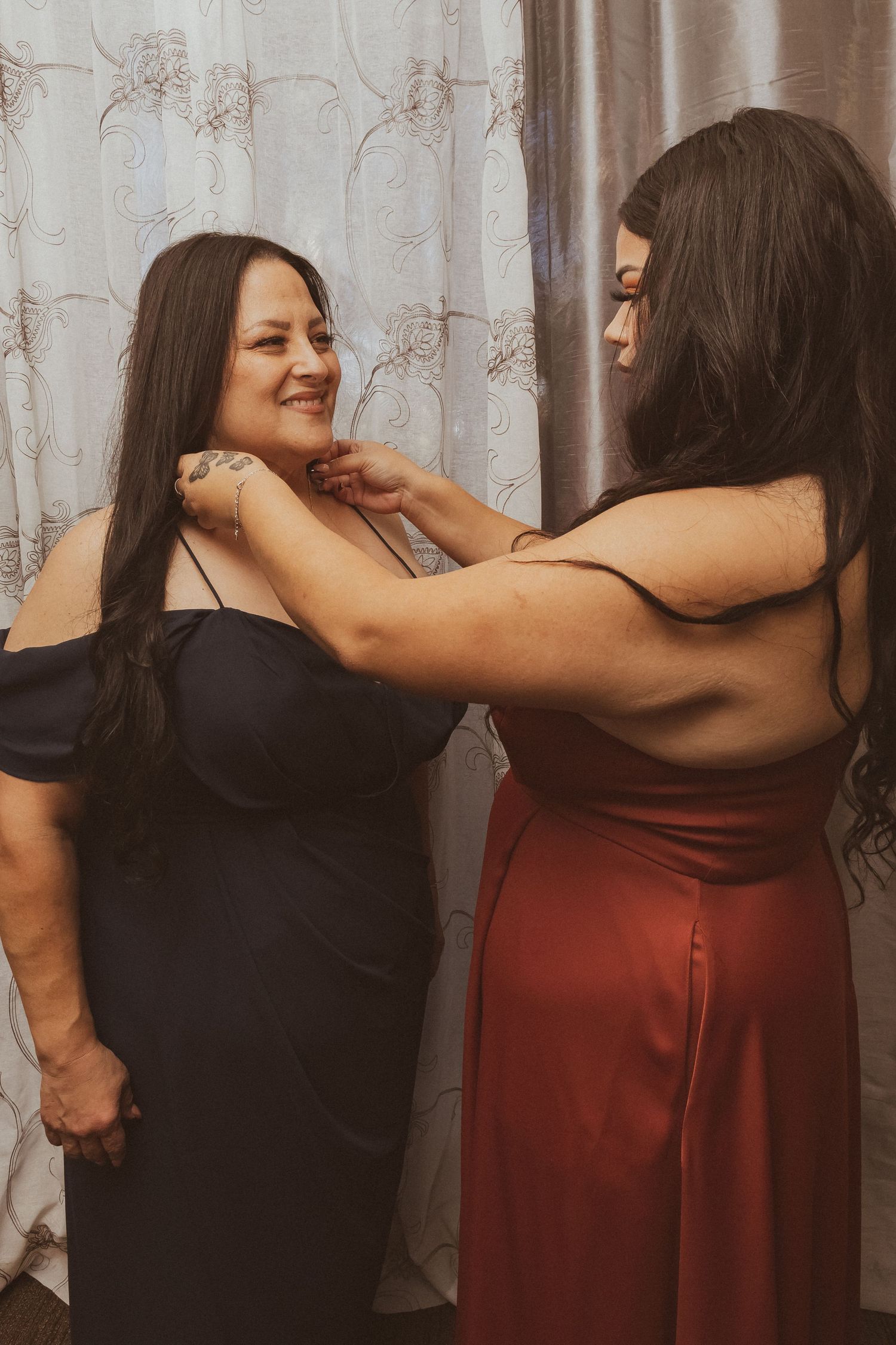 Two women in formal dresses sharing a joyful moment while getting ready together.