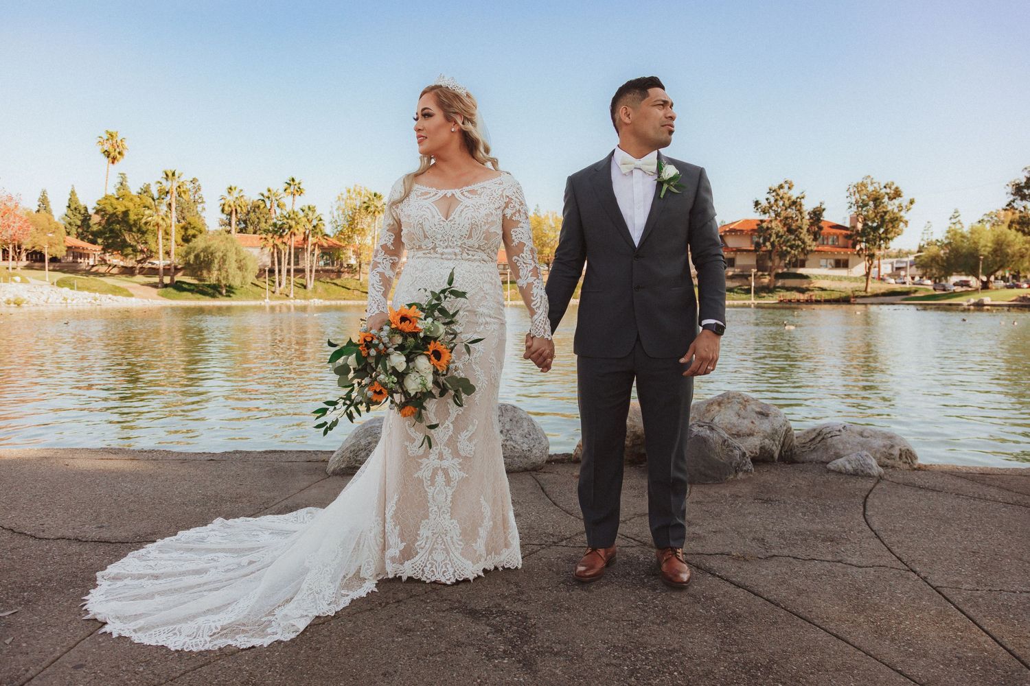 Romantic lakeside wedding photo with couple holding hands at sunset.