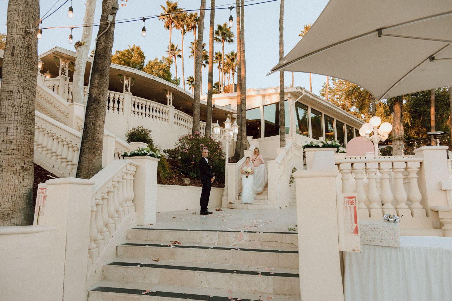 White staircase with ornate railings and palm trees at an outdoor wedding venue.