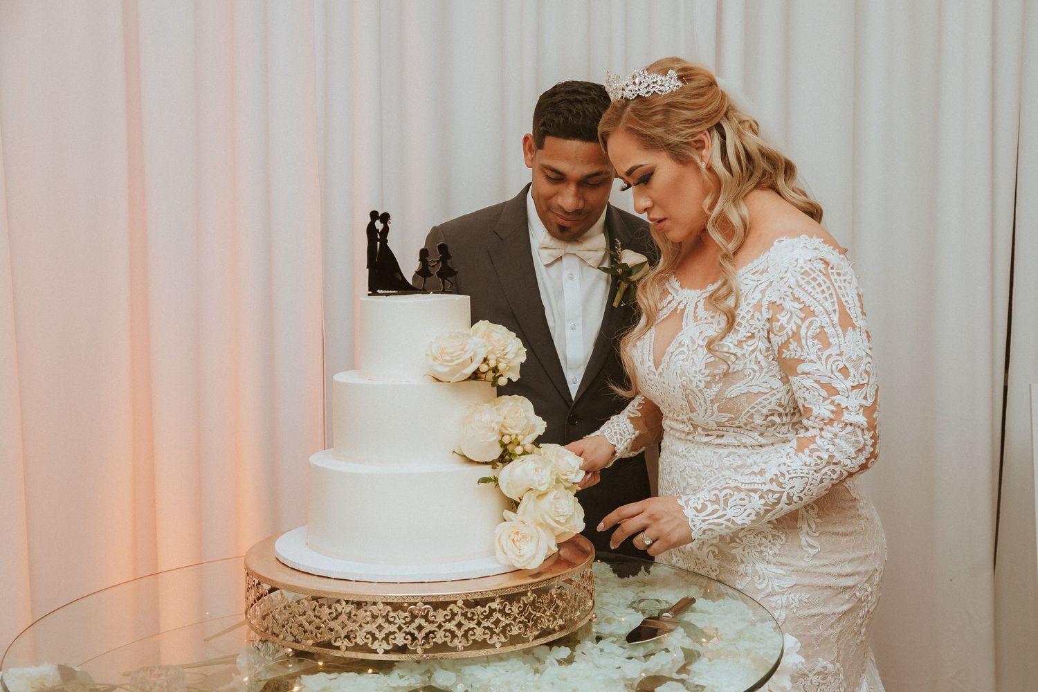 Couple sharing a moment while cutting their three-tiered white wedding cake adorned with flowers.