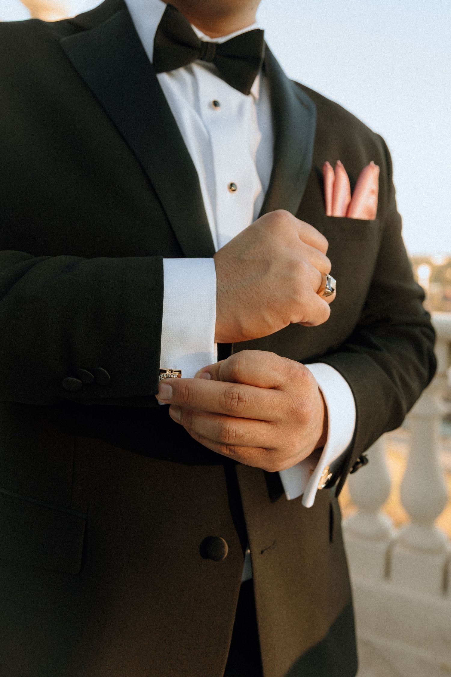 Detail shot of groom's hands adjusting sleeve with ring visible on formal black tuxedo.