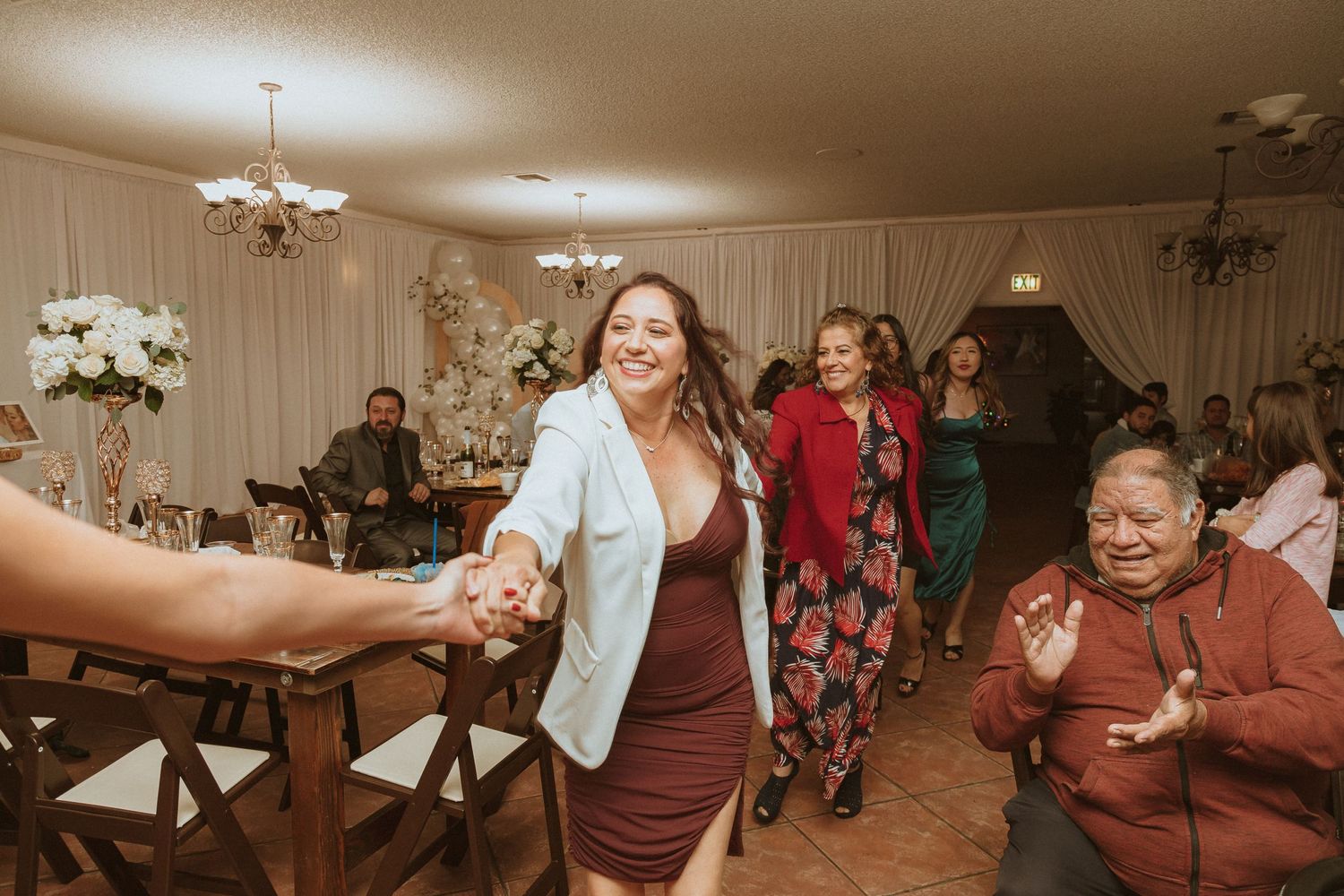 Joyful dancers holding hands in a line during a lively indoor celebration.
