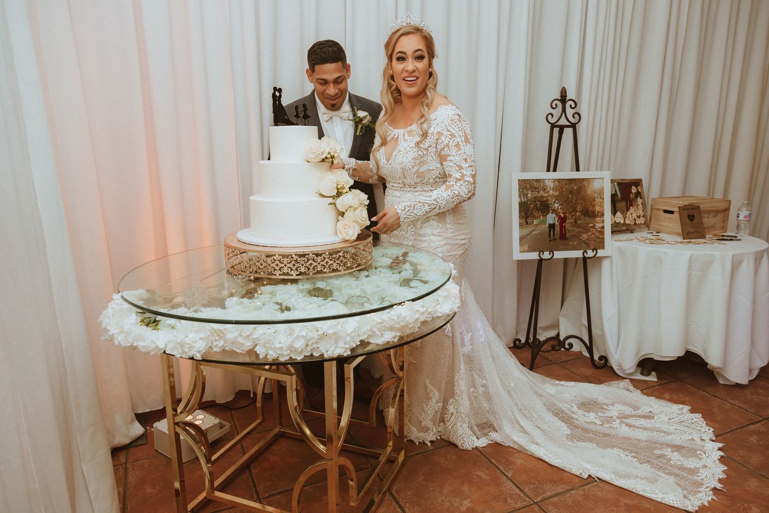 Couple poses while cutting their elegant white tiered wedding cake.