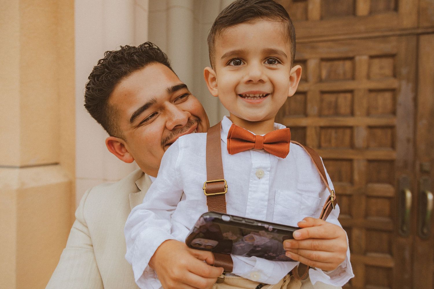 A joyful moment captured of a young boy in suspenders and bowtie holding a vintage camera.