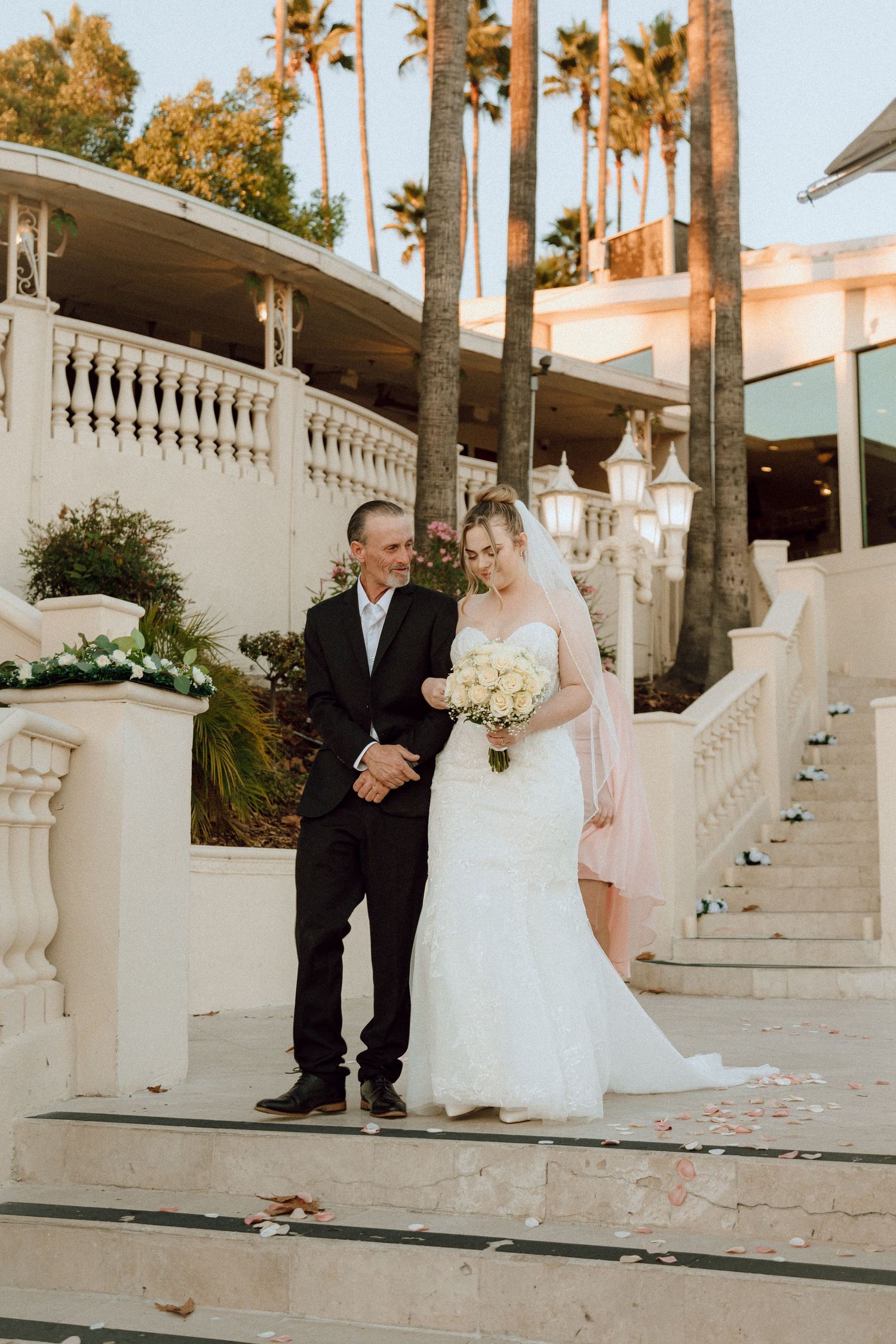 Outdoor wedding portrait on decorative white stairs with tropical palm trees backdrop.