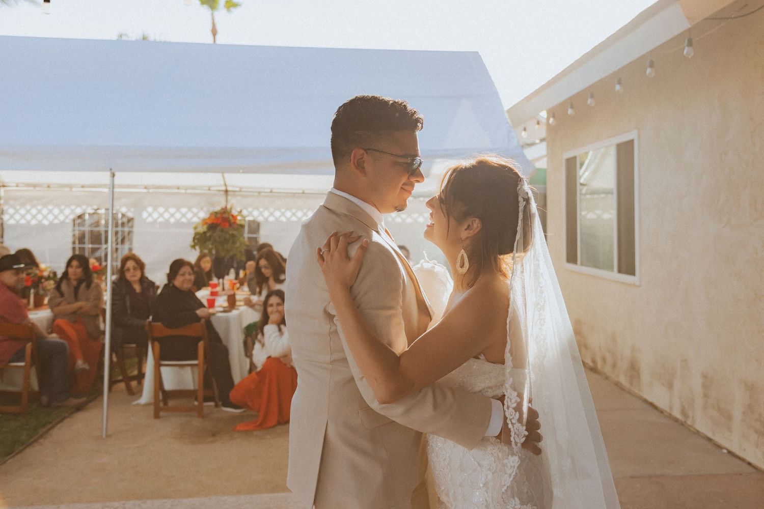 Couple shares intimate dance moment at outdoor wedding reception with guests in background.