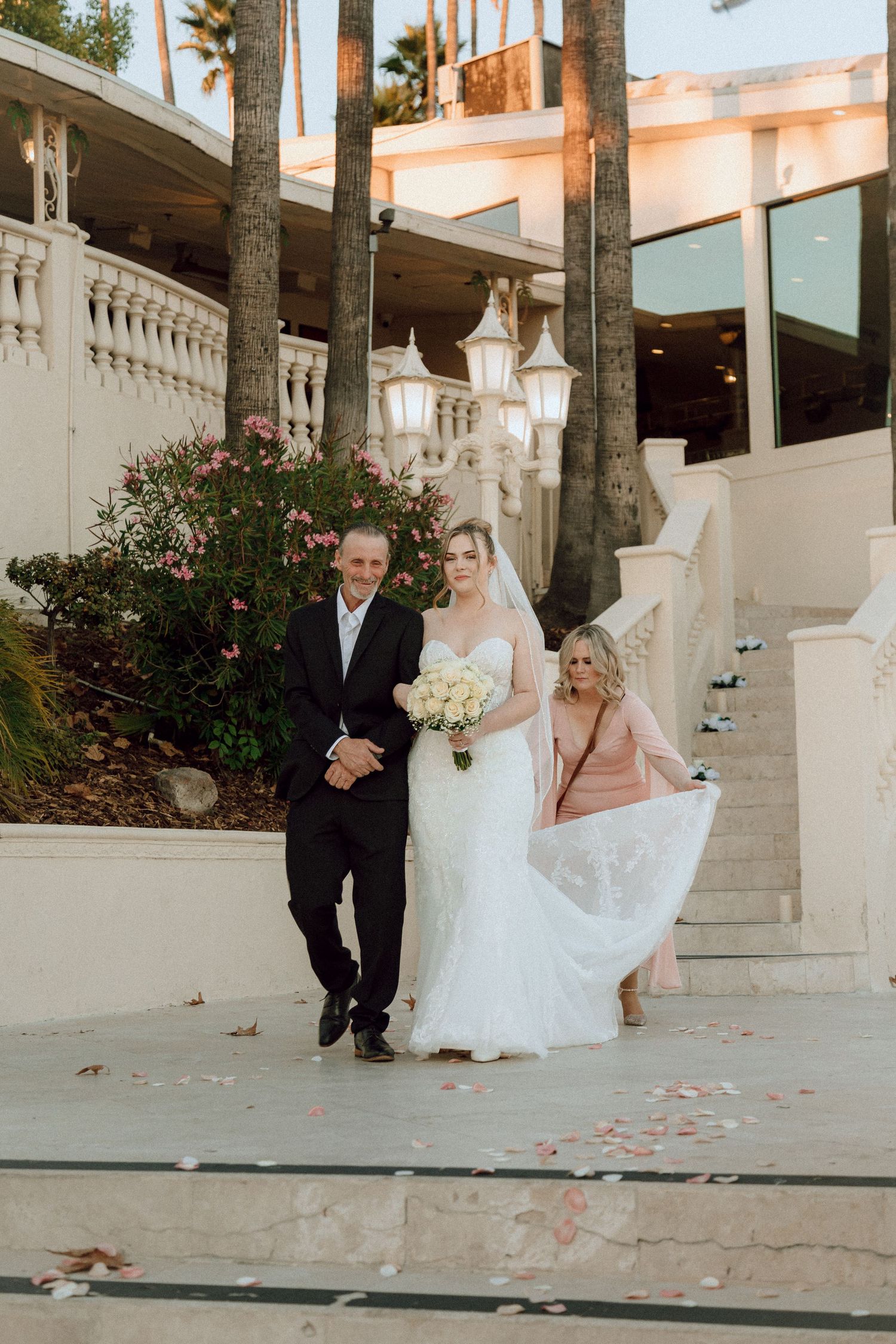 Wedding ceremony moment on grand white staircase surrounded by palm trees and lanterns.