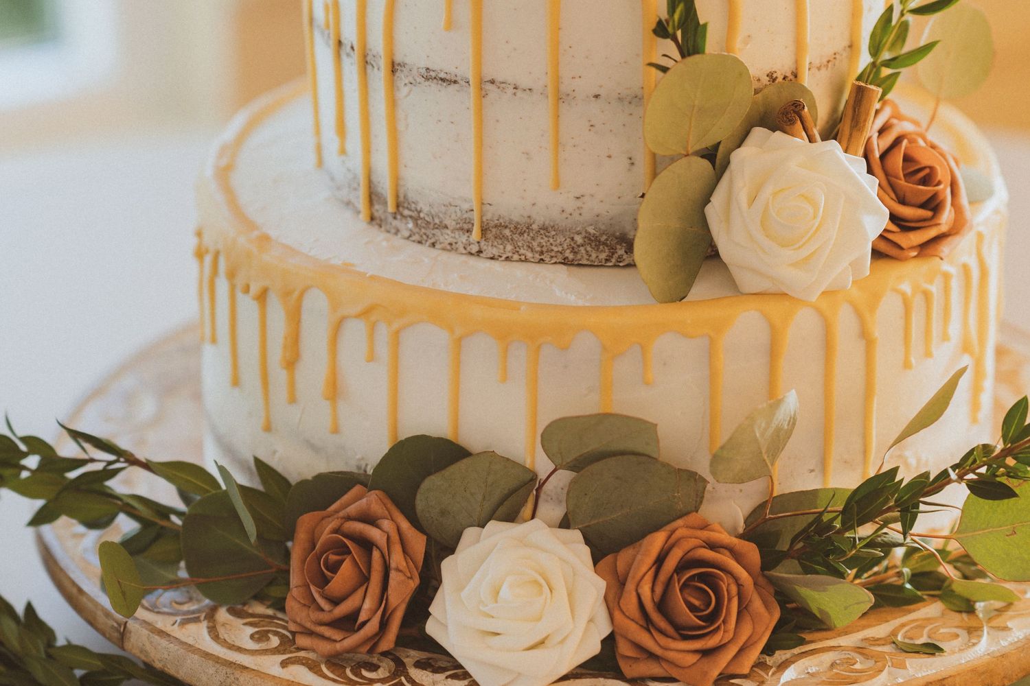 Close-up of wedding cake tiers decorated with gold drip effect and fresh roses.