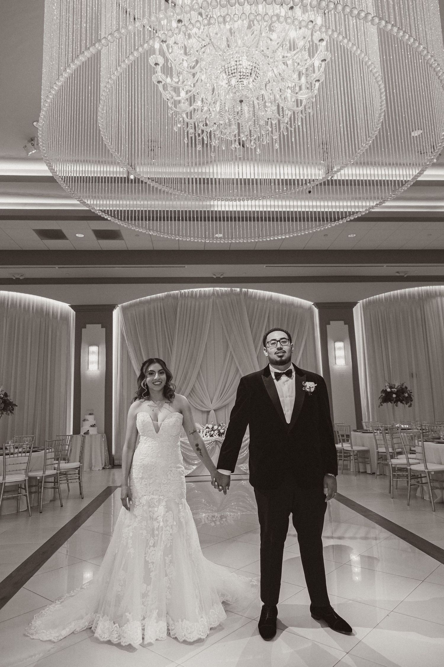 Classic black and white portrait of wedding couple standing in elegant ballroom setting.