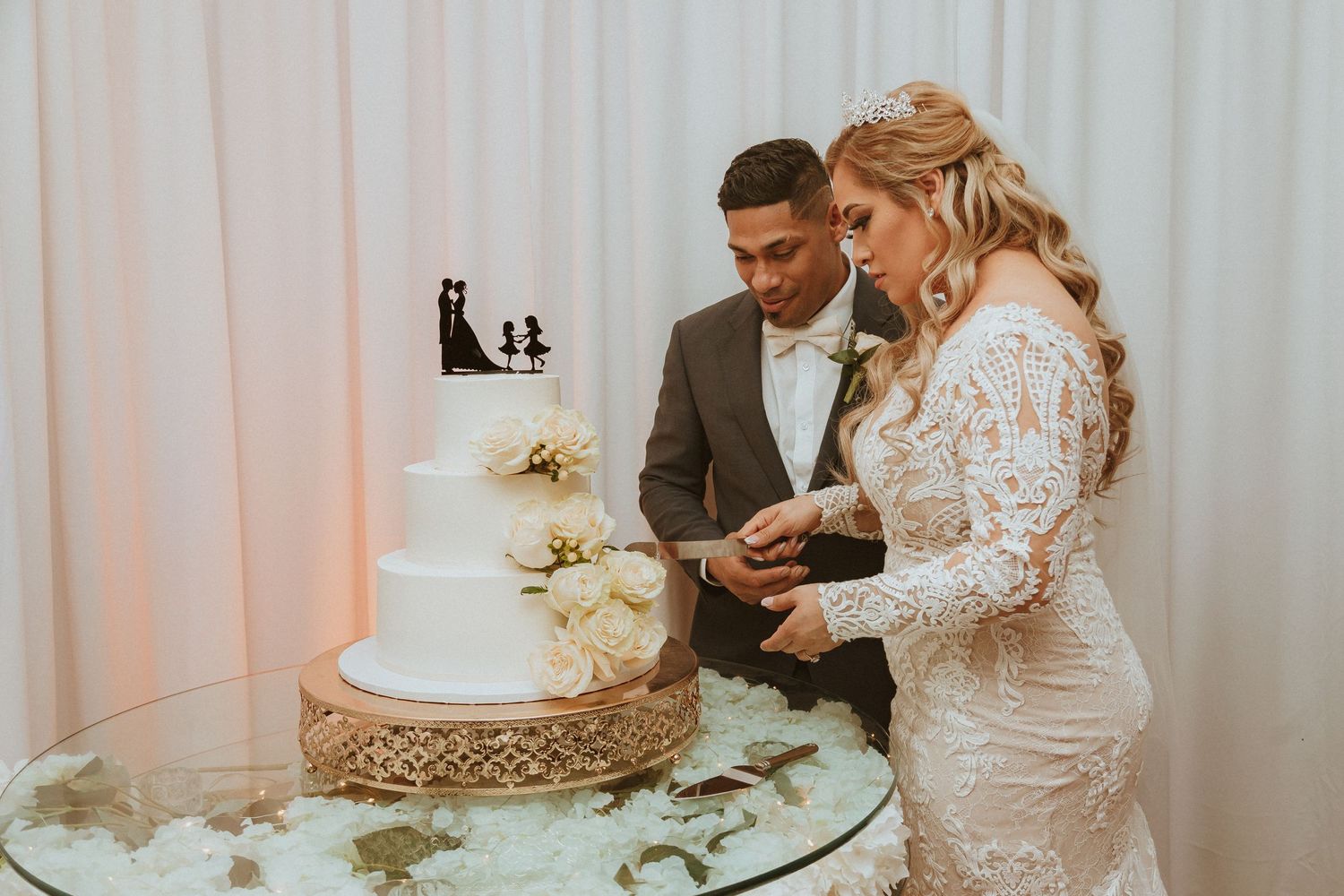 Newlyweds carefully cutting into their elegant white tiered wedding cake.
