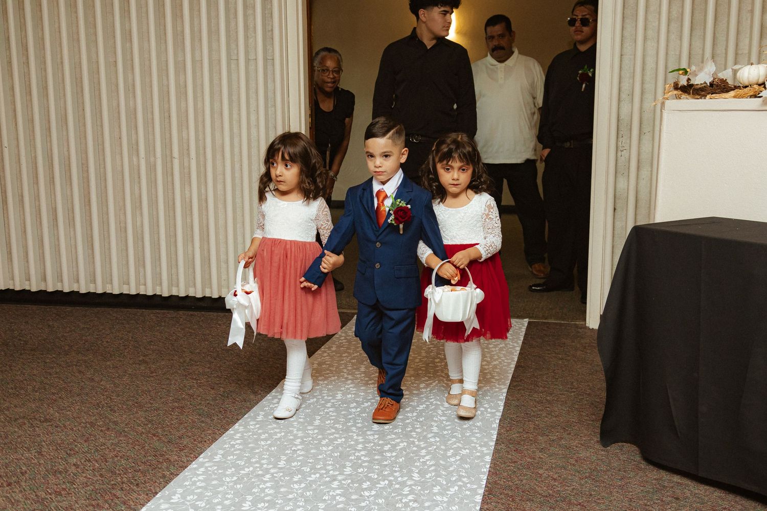 Young ring bearer and flower girls in formal attire walk down decorated aisle.