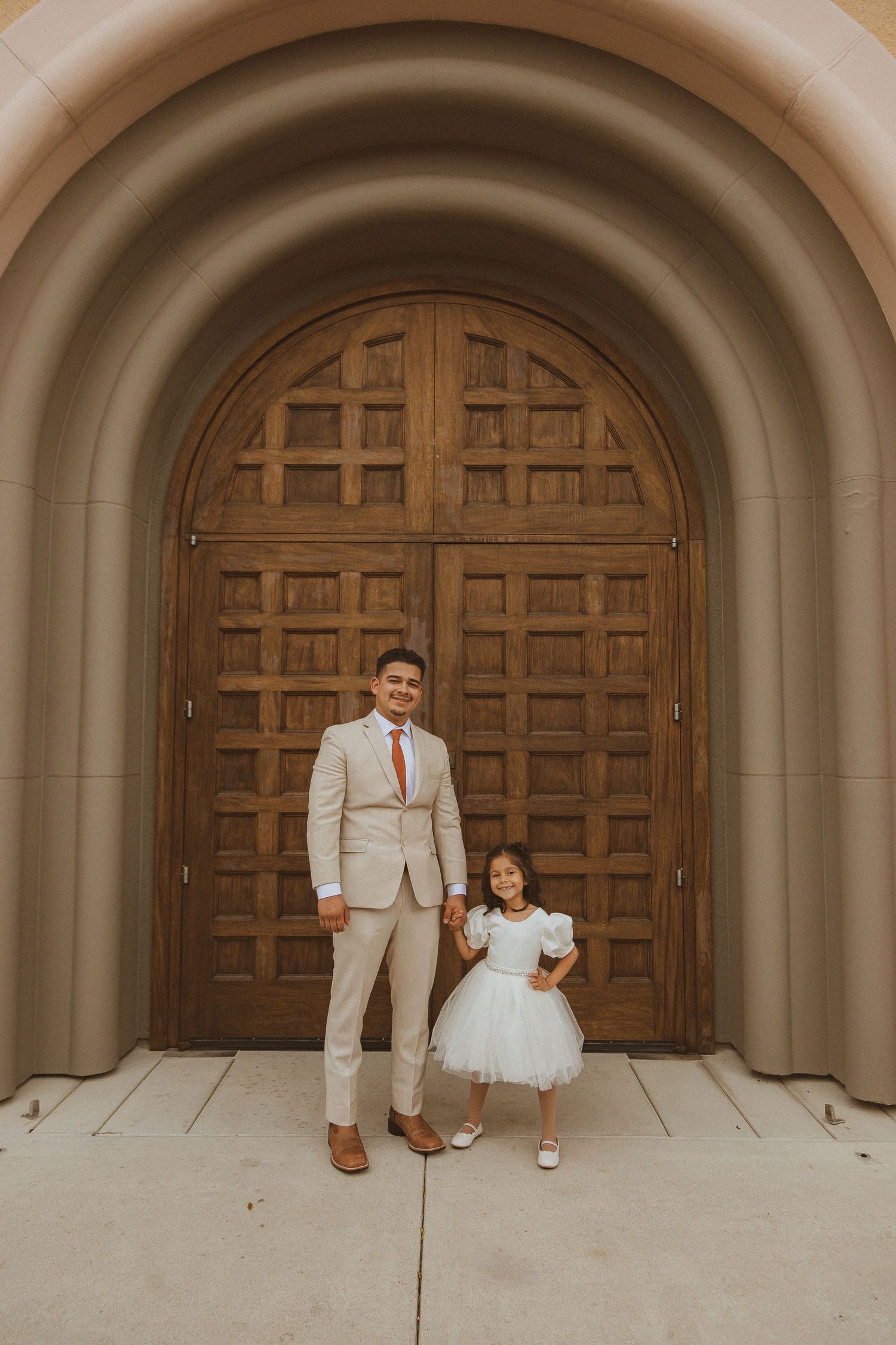 Wedding portrait against wooden church doors showing formal attire and classic architecture.