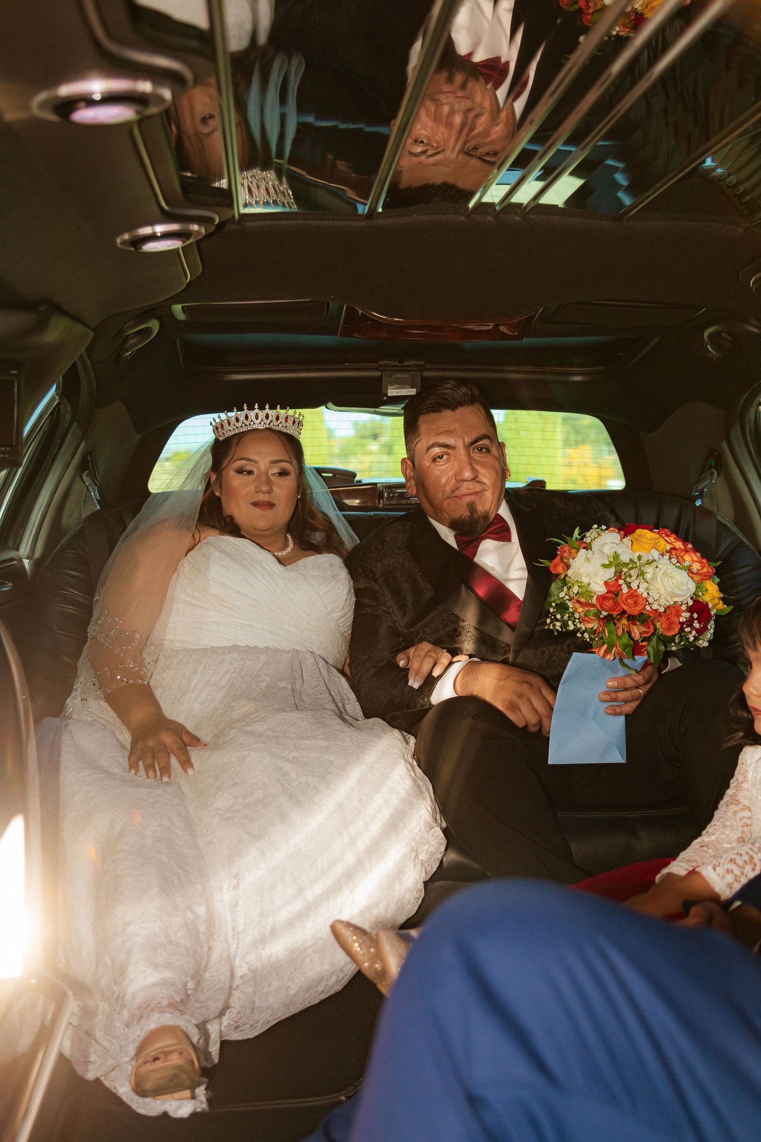 Wedding couple in formal attire sharing a candid moment inside a limousine.