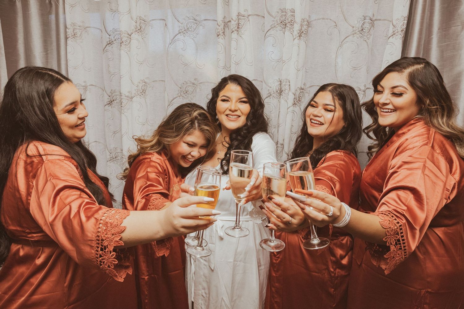 Wedding party shares a joyful champagne toast wearing matching orange silk robes.