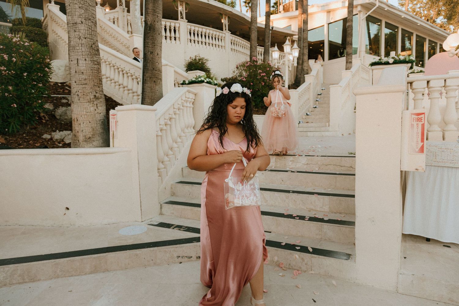 Person in pink dress poses playfully on white stone steps with string lights overhead.