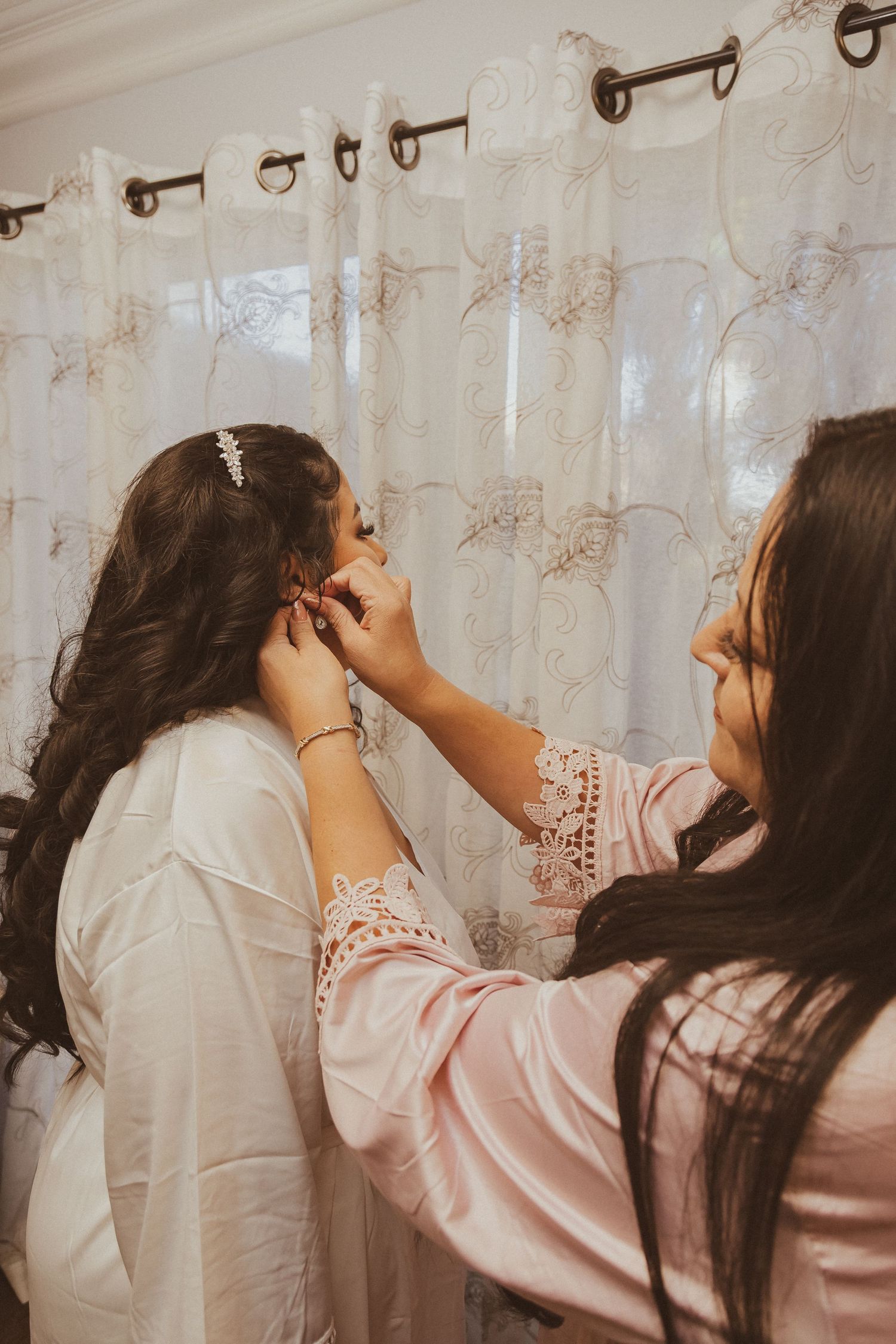 Final touches being applied to bridal makeup against a curtained backdrop.